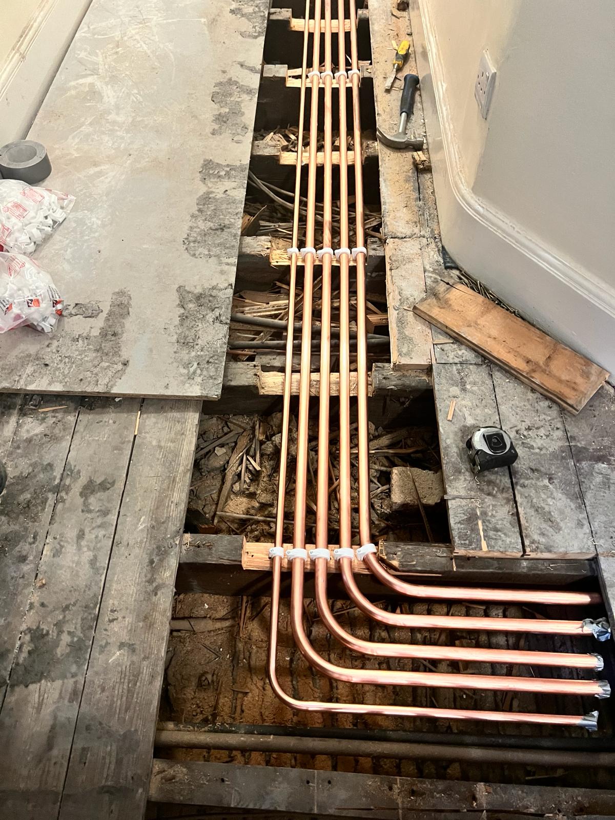 New copper central heating pipe runs installed under a lifted floorboard