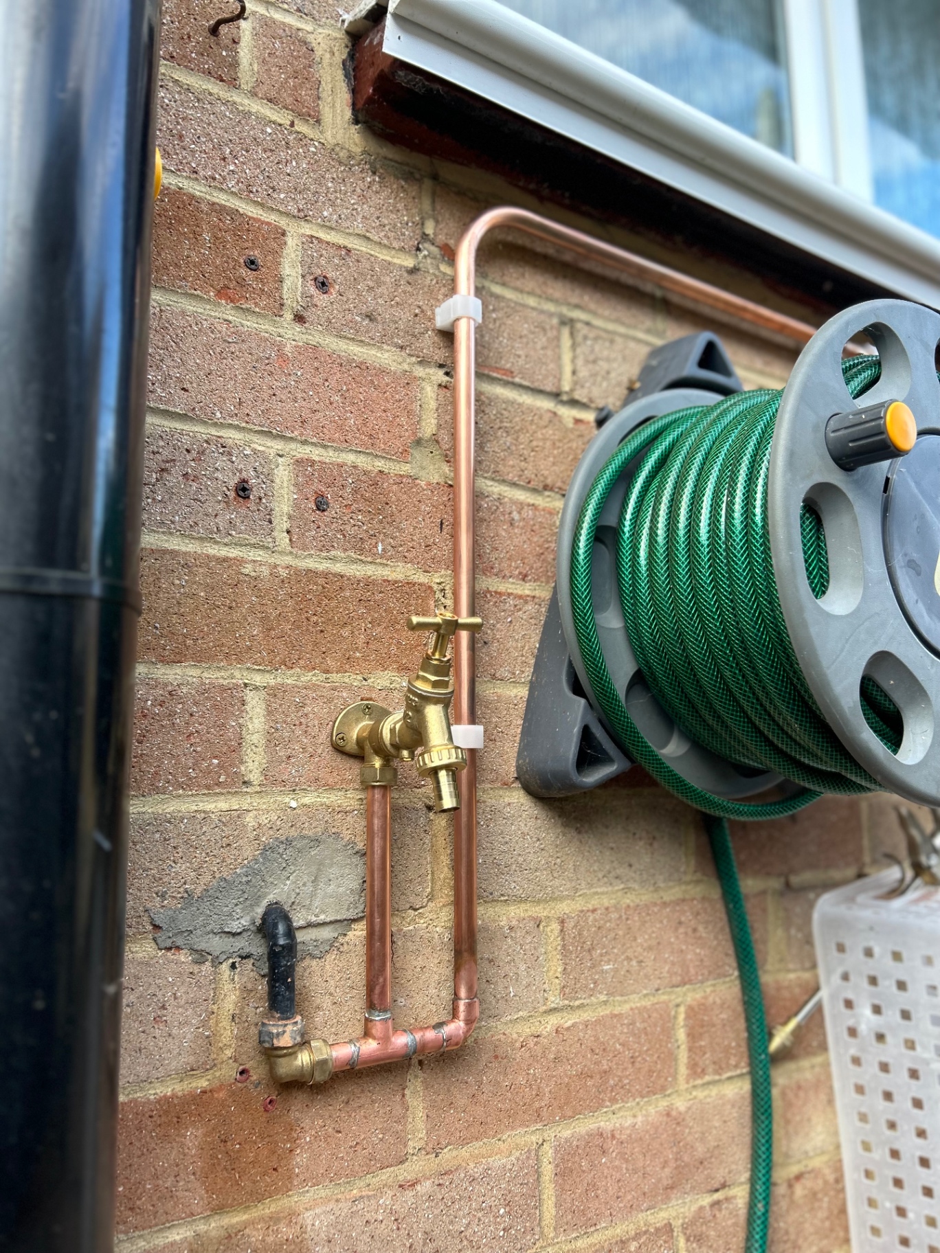 New outside tap with copper pipework beside a hose reel