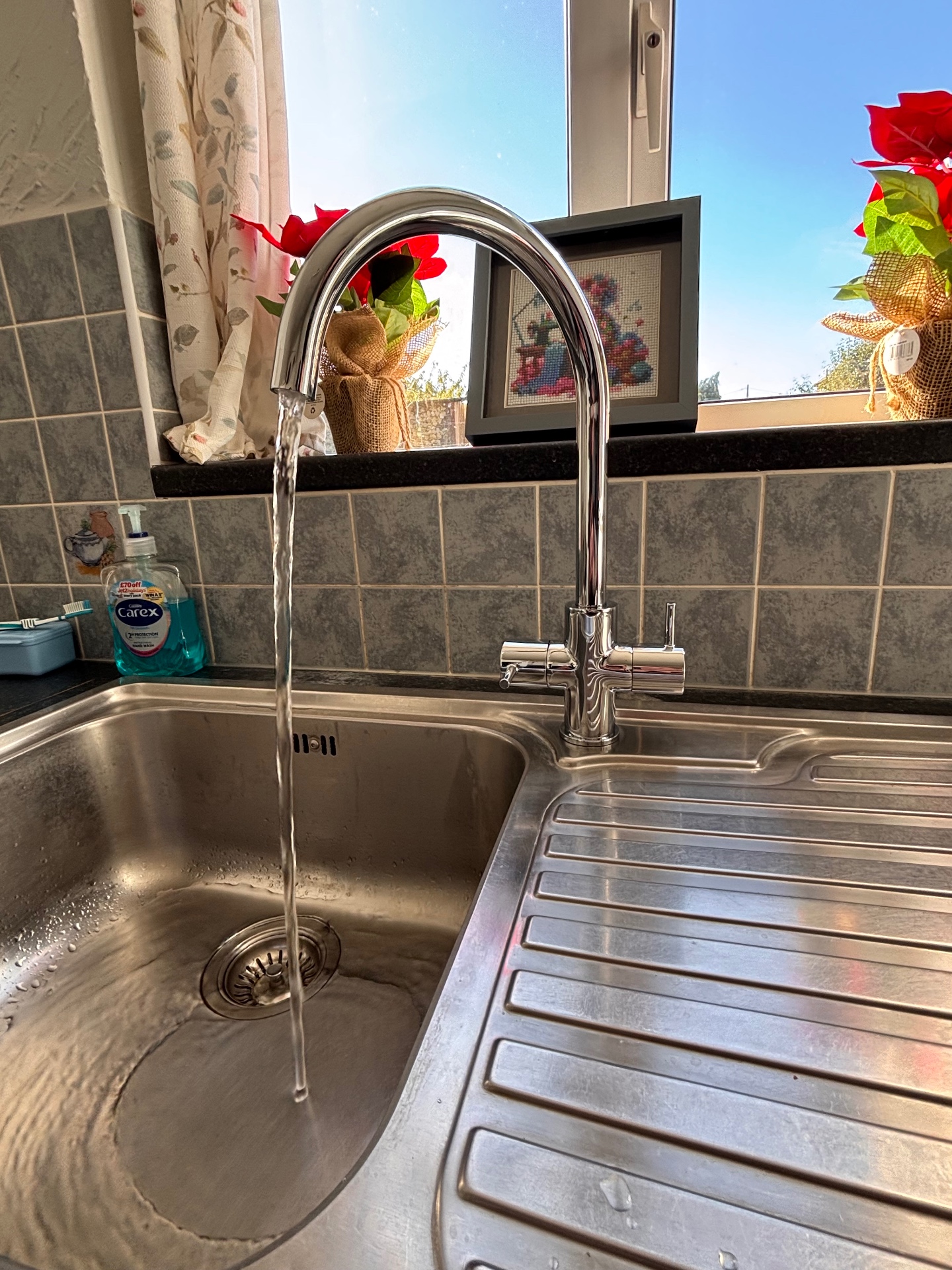 New chrome kitchen tap with water running into a stainless steel sink